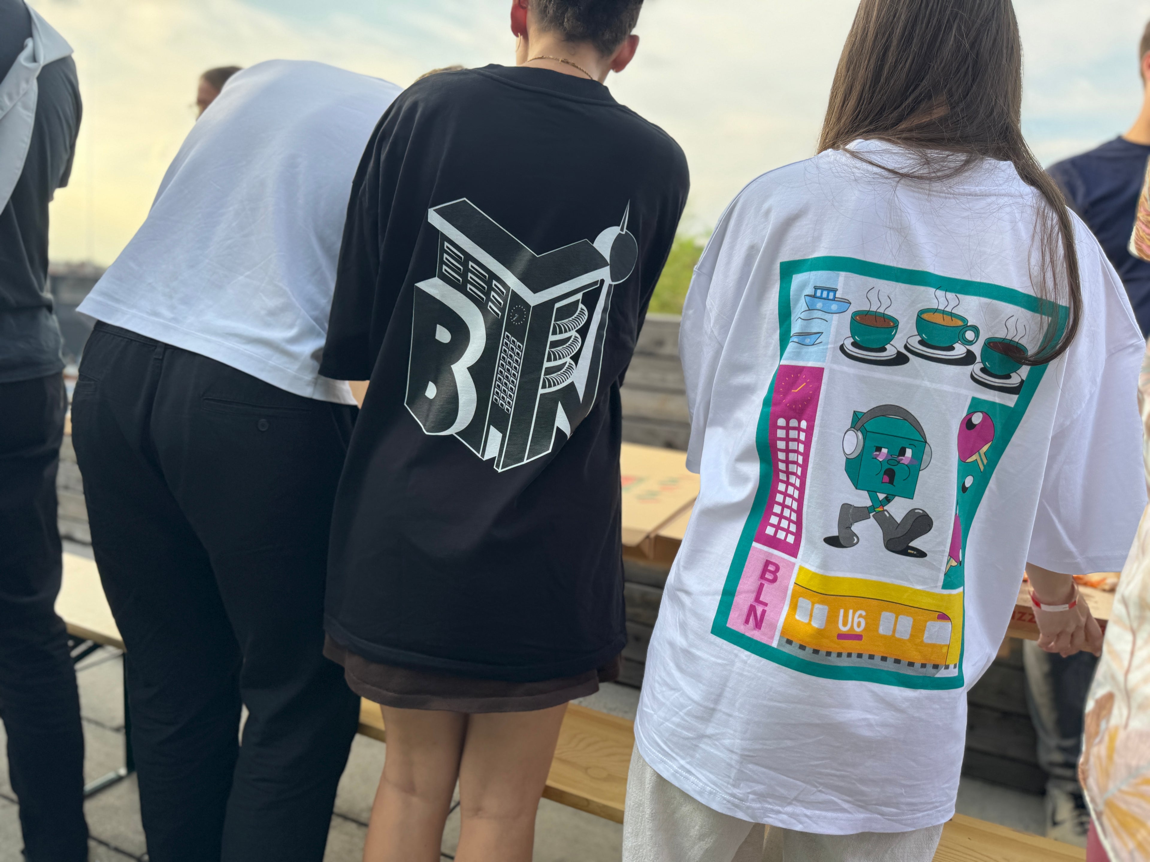 Two people wearing t-shirts with unique designs on the back, standing outdoors.