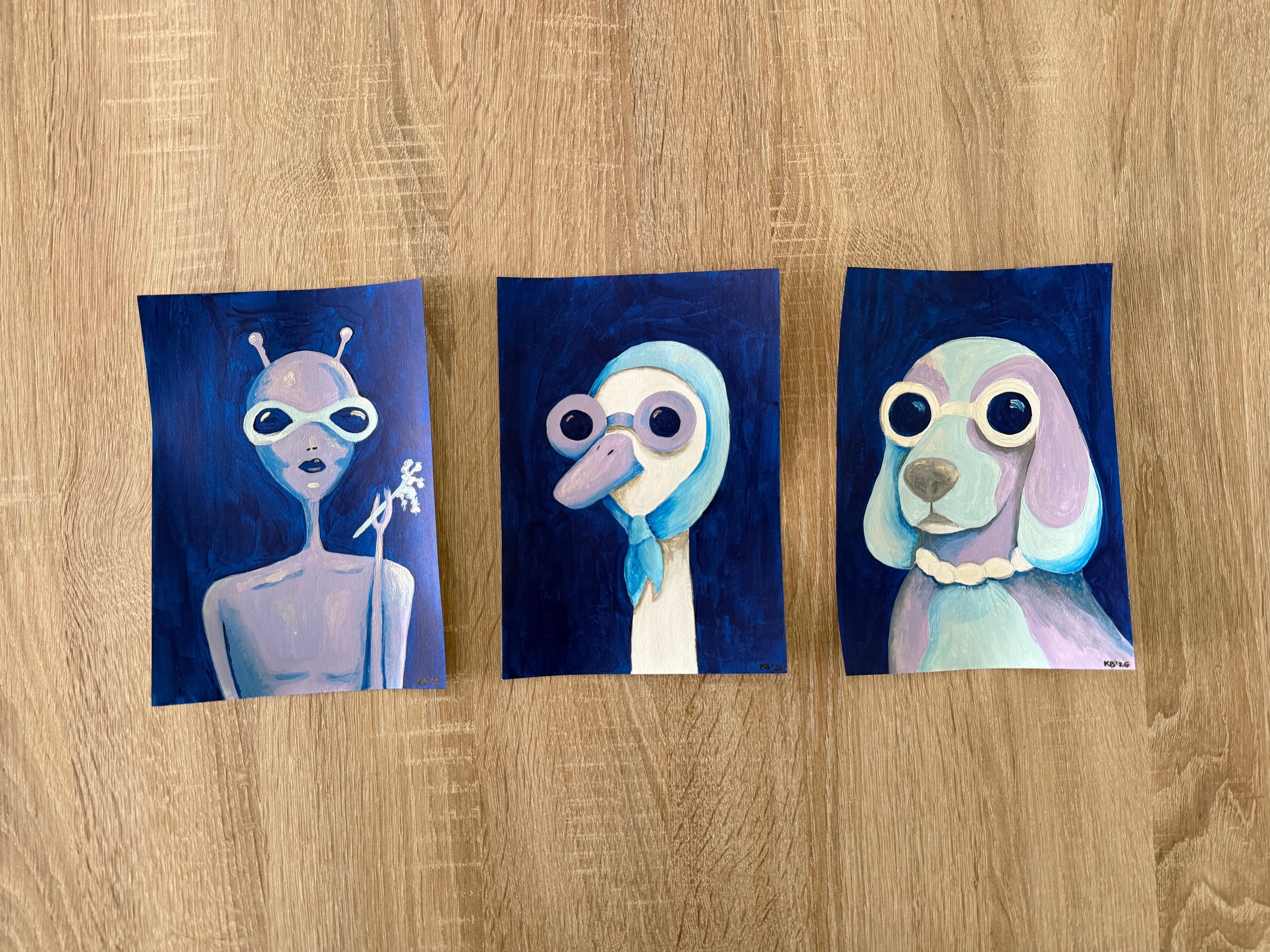 Three small paintings of cartoon characters on a wooden surface