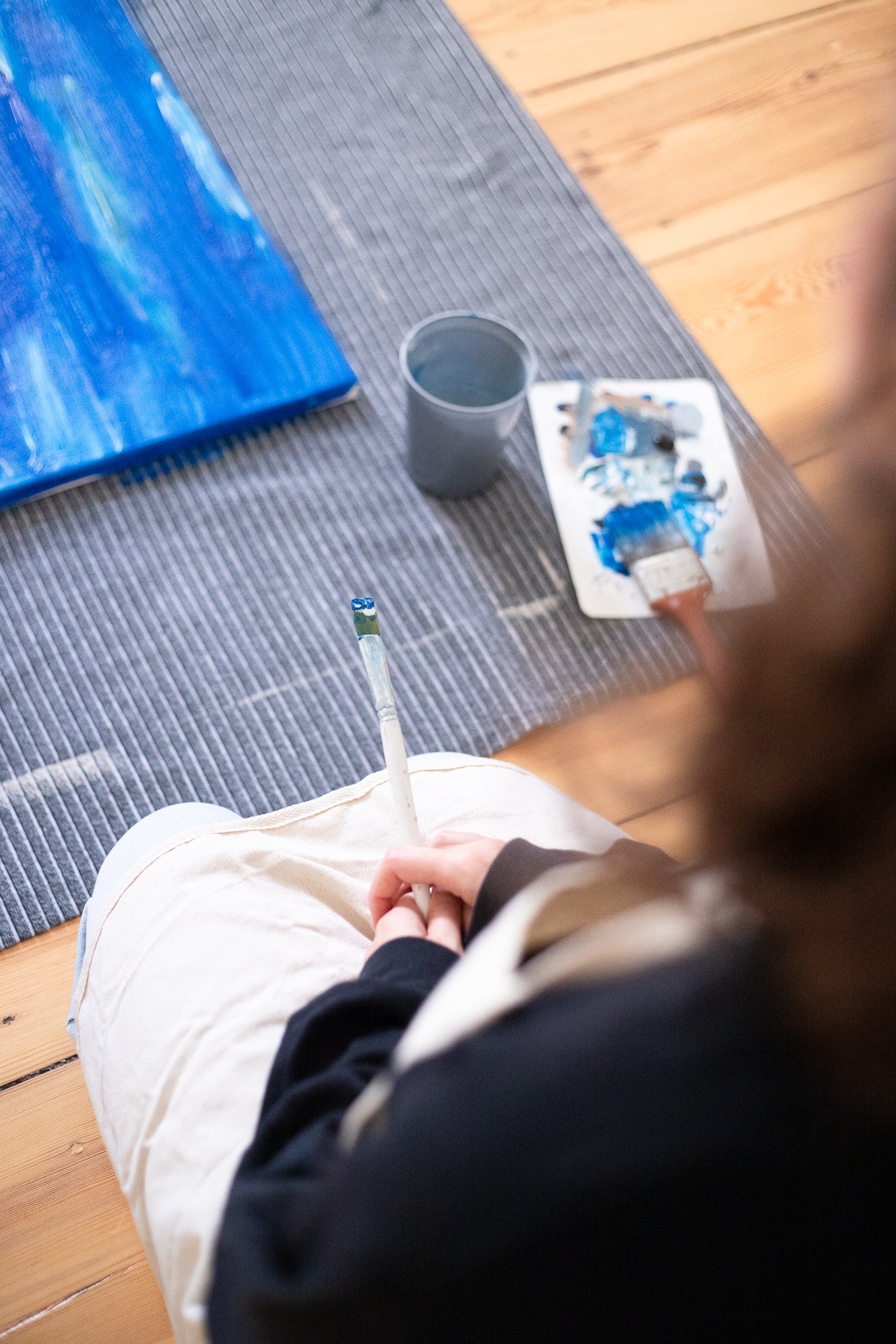 Woman looking onto a canvas on the floor with a brush in her hands