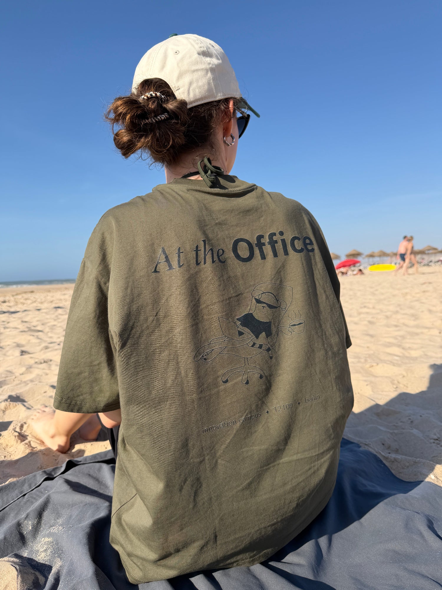 Woman at the beach wearing a custom designed shirt saying "At the office"