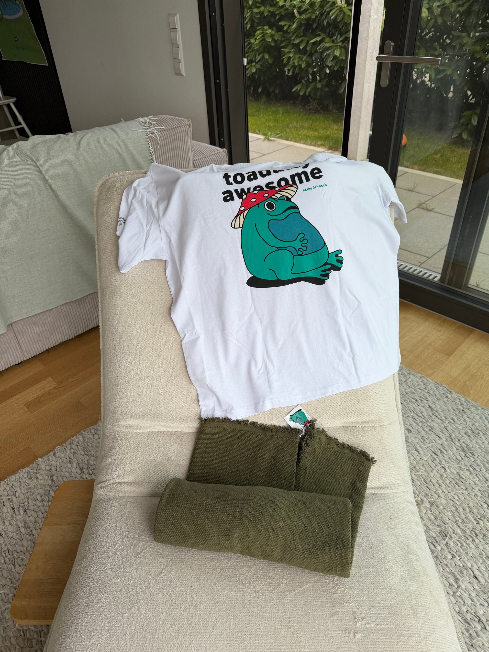 White t-shirt with a cartoon frog design on a beige chair.
